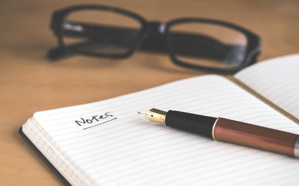 Open notebook headed "Notes" with a fountain pen and glasses (stock photo, Unsplash)